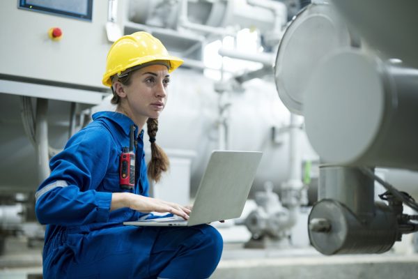 Portrait of Service Technician or engineer woman checking pressure device, Testing opening or closing valve equipment and record value in to maintance application on laptop in a factory.